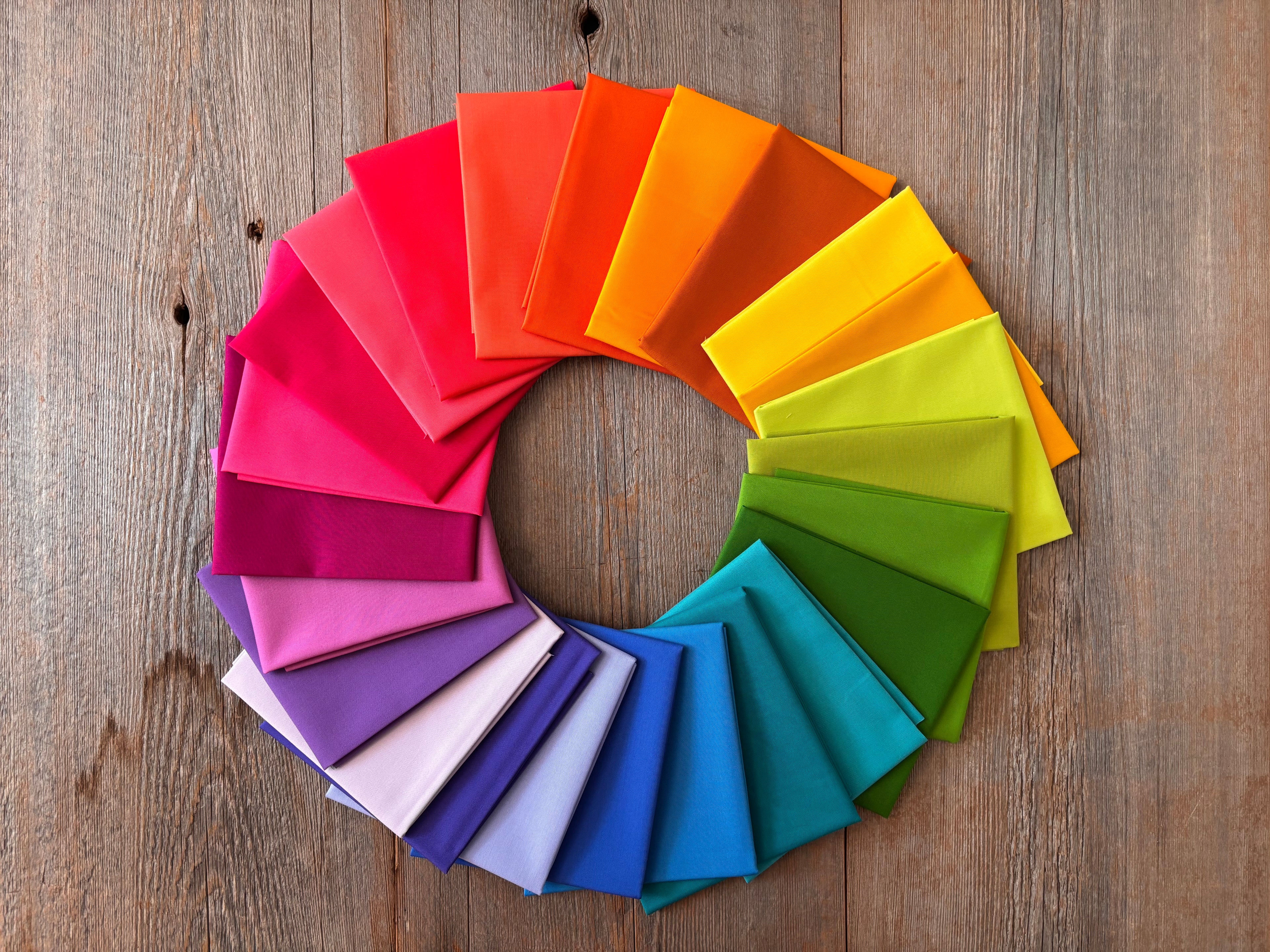 Alchemy Rainbow Fat Quarter Bundle arranged in a circular pattern on a wooden surface