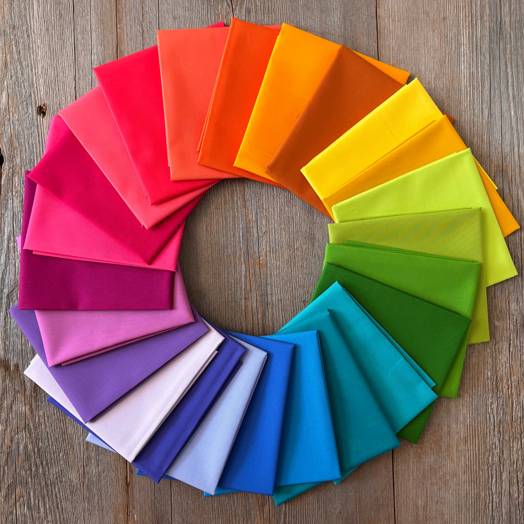 Alchemy Rainbow Fat Quarter Bundle arranged in a circular pattern on a wooden surface