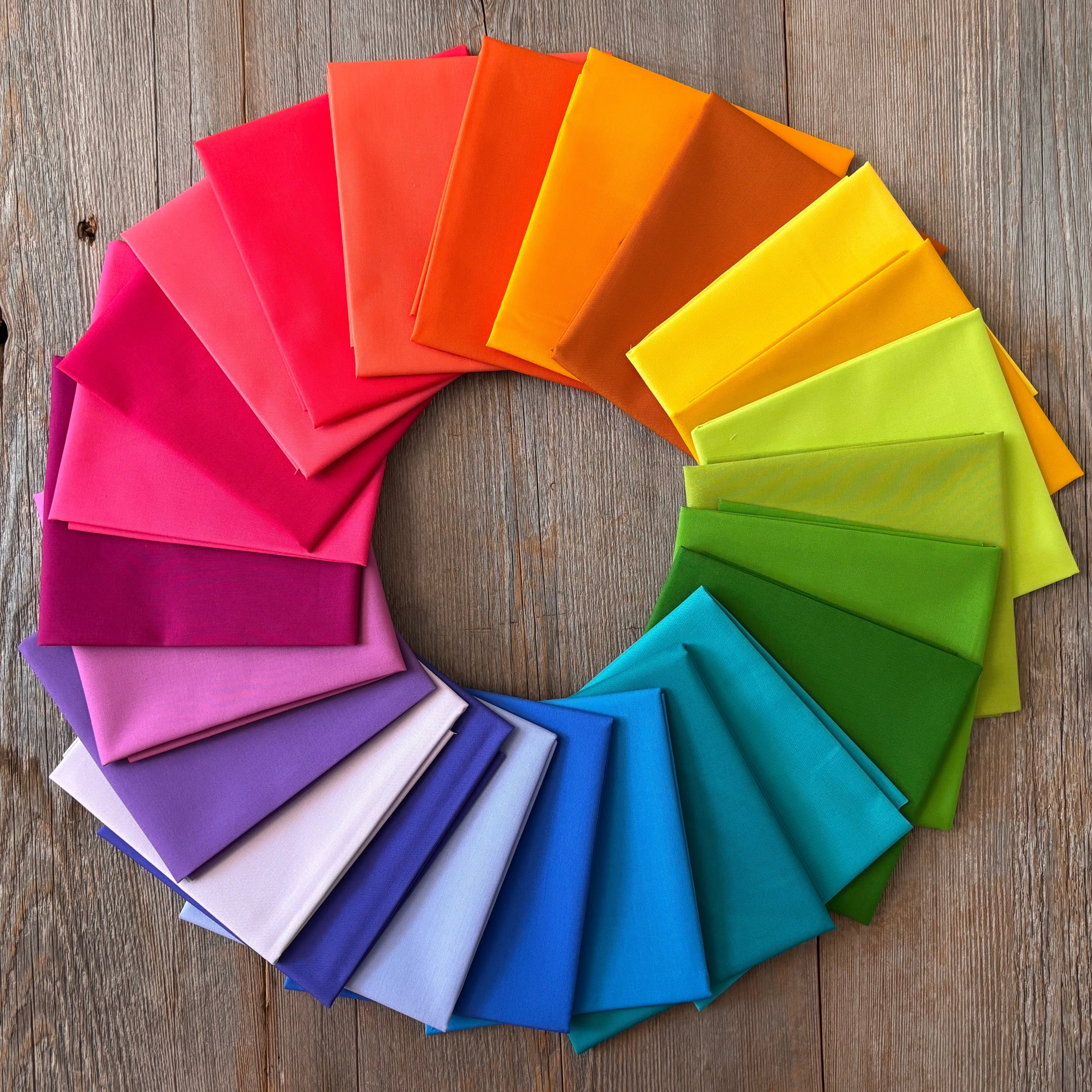 Alchemy Rainbow Fat Quarter Bundle arranged in a circular pattern on a wooden surface